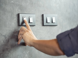 Hand reaching to turn on a modern black light switch installed on a gray wall at standard height